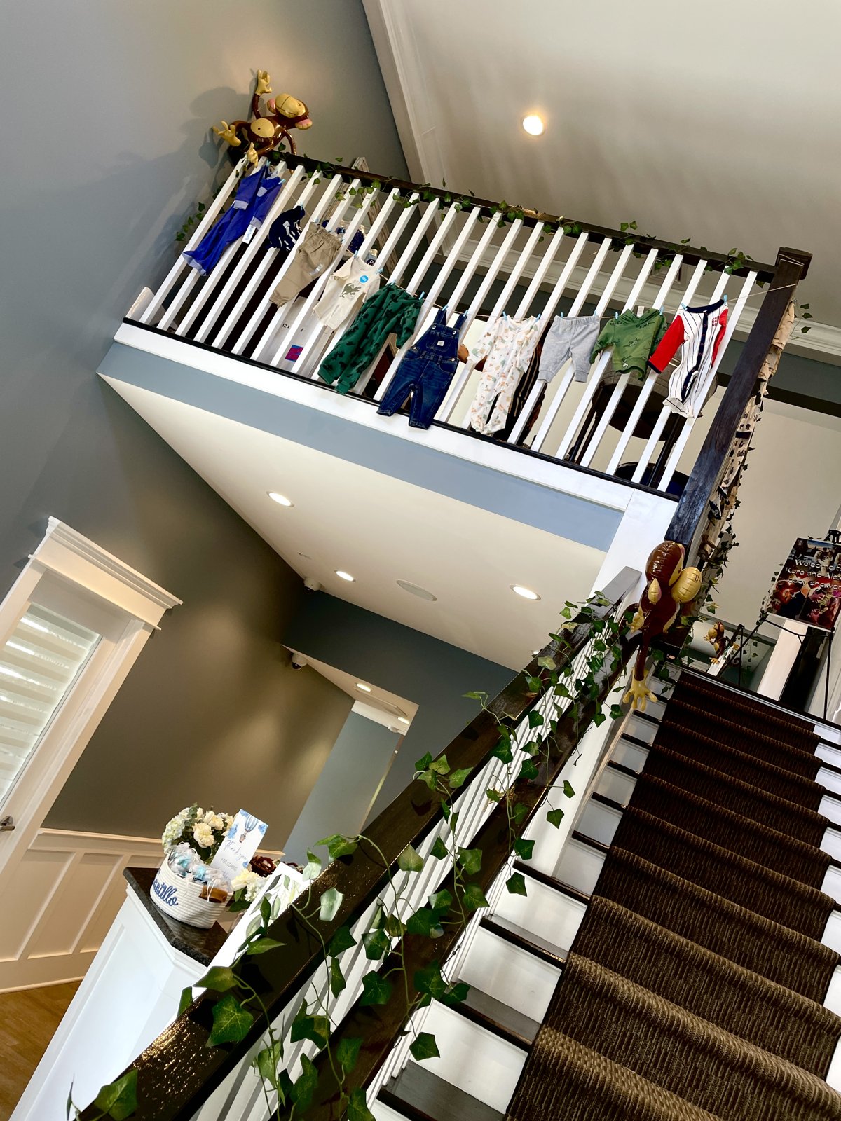 The two-story foyer decorated for a baby shower — clothesline strung along the upstairs railing, ivy on the banister