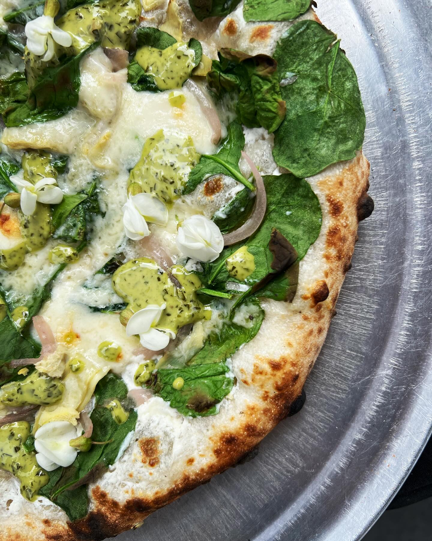White pie with spinach, pesto dollops and sprouts