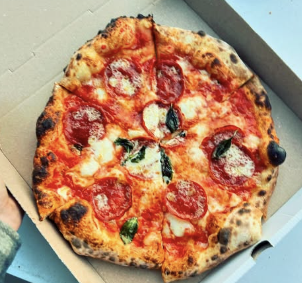 Pepperoni pizza in a cardboard box, charred crust, fresh basil