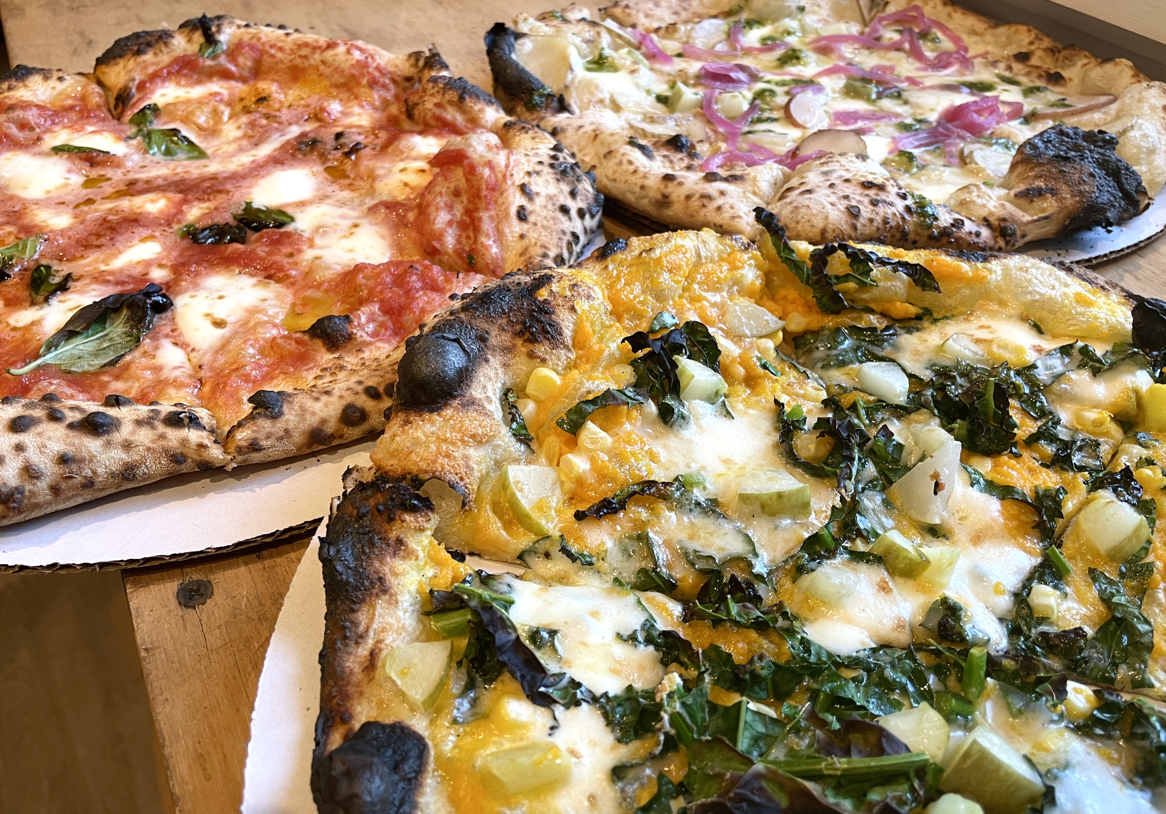 Three Neapolitan pies side by side — margherita, white with pickled onion, butternut and kale